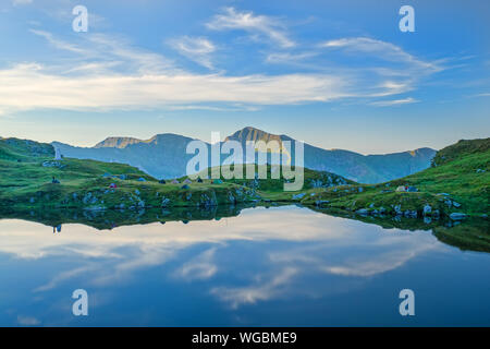 Lac calme et ciel bleu, paysage de montagne en Roumanie, de nombreuses tentes alpines au pâturage près du lac Banque D'Images