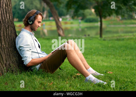En étudiant avec un casque de parc campus lire un livre. Banque D'Images