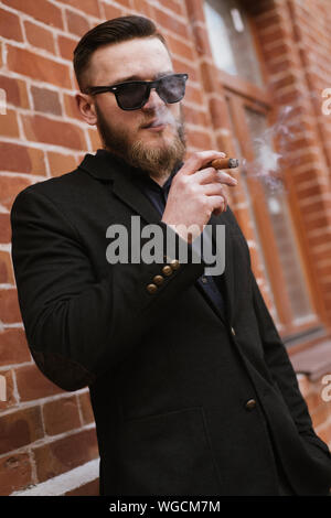 Beau barbu fumer une cigarette sur mur de brique Banque D'Images