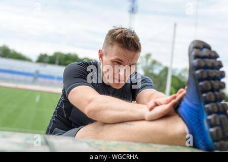 Close up shot of young male sprinter qui s'étend sur l'avant une course dans le stade. Banque D'Images