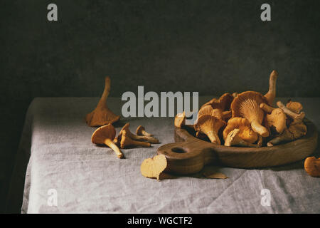 Chanterelles forêt, non cuits, crus sur planche à découper en bois avec des feuilles d'automne jaune gris sur table cloth avec mur de béton comme backgrou