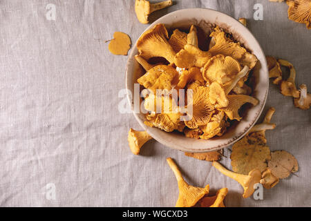 Chanterelles forestière, les matières premières en crus, Bol en céramique avec plus de feuilles d'automne jaune nappe de lin gris en arrière-plan. Mise à plat, de l'espace Banque D'Images