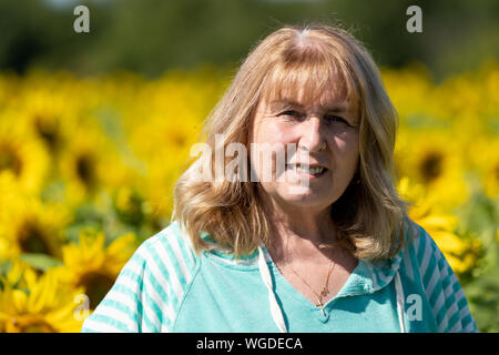 Femme Senior (60-65 ans) pose devant un champ de tournesols Banque D'Images