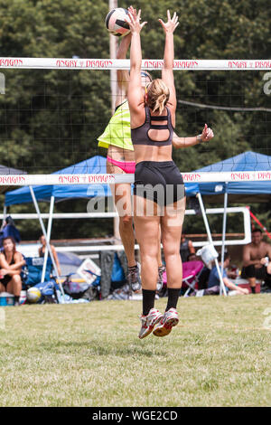 Une femme saute haut pour spike ball comme adversaire essaie de le bloquer dans un tournoi de volley-ball de l'herbe tripler le 25 août 2019 à Doraville, Géorgie. Banque D'Images