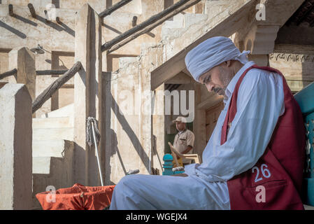 Doha, Qatar - 3 Dec 2016 : un porteur est en attente de son quart de travail pour commencer, tandis qu'un autre employé souk est de passage. Prises dans le souk Wakif, Doha Banque D'Images