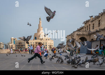 Doha, Qatar - 25 Nov 2016 : Jeune garçon courir après un grand nombre de pigeons. Prises sur la fin de l'automne jour après-midi dans le souk Wakif, Doha Banque D'Images