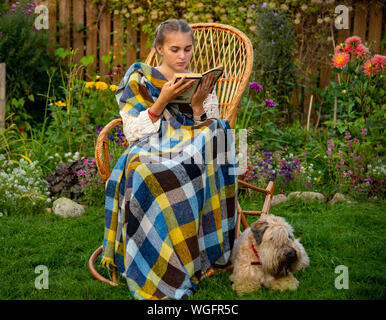 Belle fille assise dans un fauteuil à bascule en osier avec un livre.à côté du chien. Banque D'Images