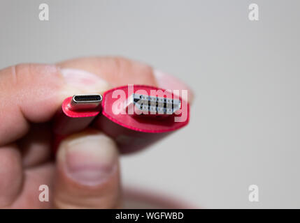 Close up of a man's main gauche tenant une clé usb type c pour câble HDMI avec broches en face de l'objectif. Banque D'Images