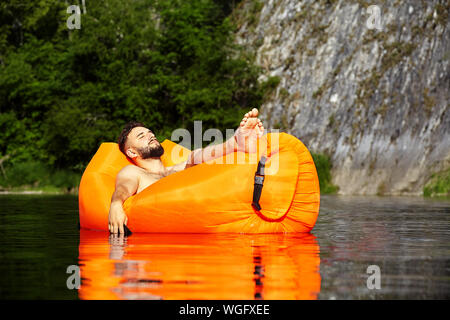 L'homme s'est endormi dans un radeau à la dérive le long de la rivière et laissa tomber sa main avec le téléphone étreint dans dans l'eau. A l'intérieur de l'eau Banque D'Images