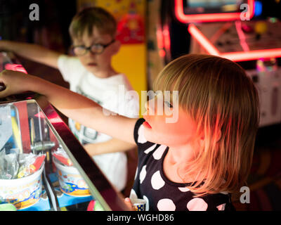 A 4 ans fille blonde joue 2p coin slot machines dans une ville balnéaire arcade avec 5 ans d'une sœur. Banque D'Images