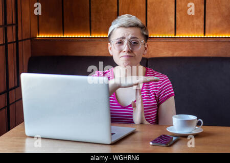 Time out ! Portrait d'avertissement triste charmante fille indépendant avec des cheveux courts blonde est assise dans un café et à la recherche à l'appareil photo avec les bras levés un Banque D'Images