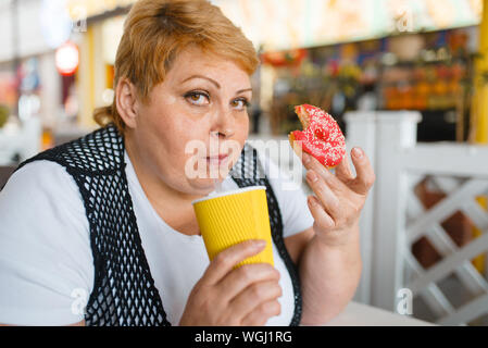 Fat Woman eating donuts au restaurant fast-food Banque D'Images