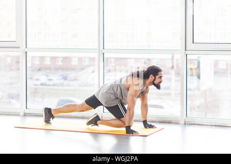 Portrait de beau jeune homme musclé adultes avec de longs cheveux bouclés dans les vêtements de sport sur le tapis jaune abs faisant de l'exercice pour les muscles de ton ventre. Piscine, win Banque D'Images