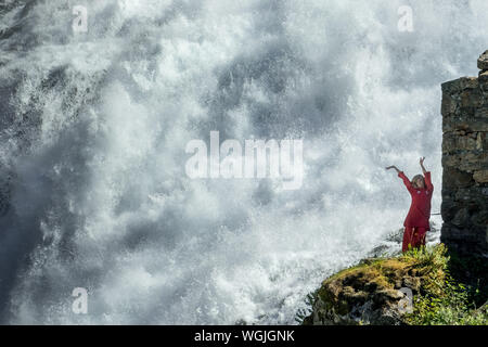 Femme habillée en rouge est une fée, Huldra, saga figure, cascade Kjosfossen, chute près de Fureberget, danseuse en robe rouge, parois rocheuses, Flåm, Sogn og Fjo Banque D'Images