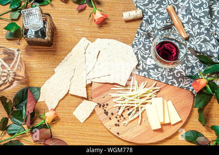 La vie toujours avec différentes variétés de fromage sur la plaque en bois avec des copeaux de pain, un verre de vin, des roses, du vin tire-bouchon Banque D'Images