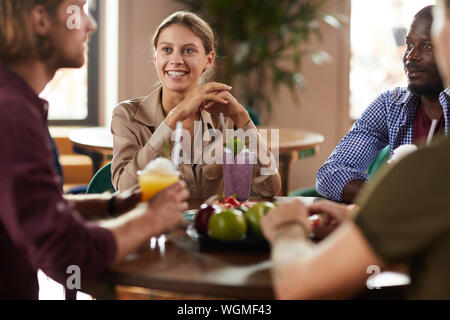 Multi-ethnic group of friends enjoying déjeuner ensemble assis à table dans un café, l'accent sur smiling young woman, copy space Banque D'Images