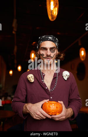 Taille portrait d'adult man wearing pirate costume posing holding pumpkin pendant Halloween party in nightclub, copy space Banque D'Images