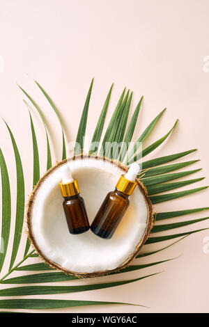 L'huile de noix de coco en bouteille à ouvrir les noix et la pâte en pot, feuille de palmier vert arrière-plan. Les produits cosmétiques naturels. Banque D'Images