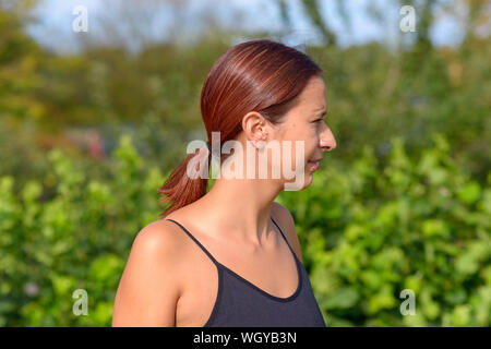 Jolie femme à côté à l'extérieur dans le soleil d'été regarder quelque chose hors cadre à droite Banque D'Images