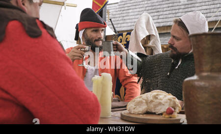 Vue de l'épaulement de deux chevaliers assis à la table et de trinquer avec tasse. Des hommes habillés en tenue médiévale. Banque D'Images