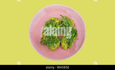 Deux tranches de pain grillé garni de purée d'avocat à la roquette salade de roquette fraîche ou sur une plaque rose contre un fond vert lime Banque D'Images