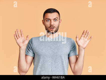 Jeune homme choqué avec les bras jusqu'à la caméra en étonné sur fond jaune. Concept d'émotions Banque D'Images