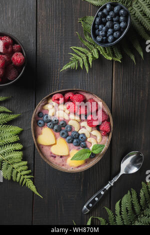 Petit déjeuner tropical sain et bananes smoothie bleuet décoré de fruits dans un bol de noix de coco sur un parquet en bois sombre. Vue de dessus. Manger propre, ve Banque D'Images
