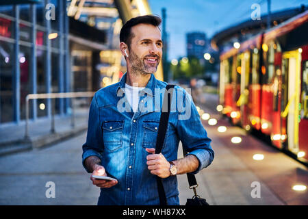 L'homme écoute de la musique en attendant le tram au cours de la navette du soir après le travail Banque D'Images