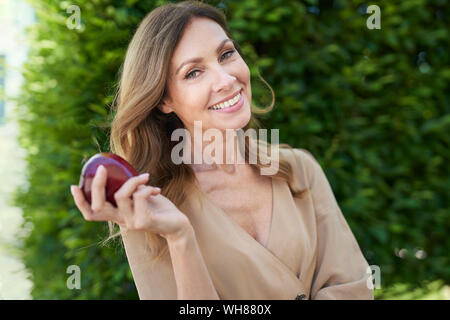 Portrait of young woman holding an Apple, d'une haie à l'arrière-plan Banque D'Images