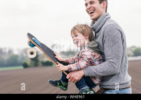 Père et fils s'amuser, jouer avec la planche à roulettes à l'extérieur Banque D'Images