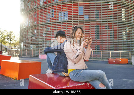 Couple assis dos à dos l'utilisation de téléphones cellulaires, Barcelone, Espagne Banque D'Images