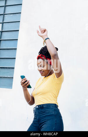 Smiling young woman listening music avec casques et d'écouteurs en face de mur blanc Banque D'Images