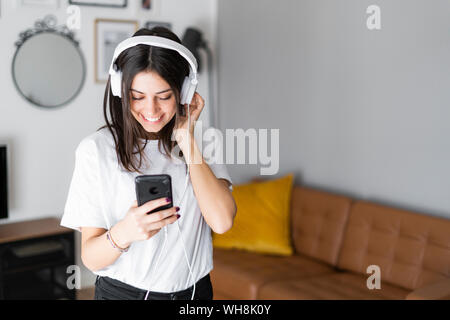 Happy young woman with smartphone et casque à la maison Banque D'Images