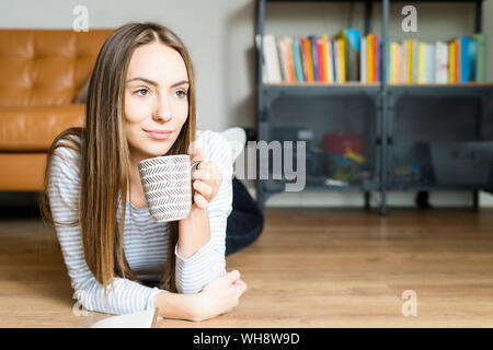 Ambiance jeune femme allongée sur le sol à la maison à boire du café Banque D'Images