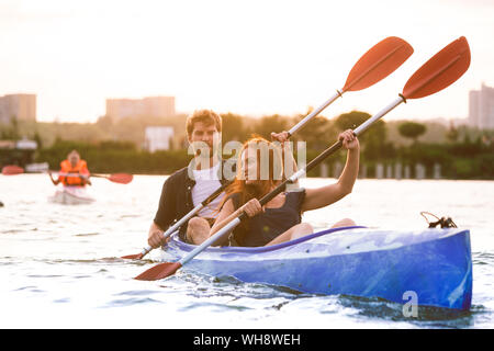 Certain young caucasian couple kayak sur rivière avec coucher du soleil dans l'arrière-plan. Avoir du plaisir dans l'activité de loisirs. Romantique et heureux homme et femme sur le kayak. Le sport, les relations concept. Banque D'Images