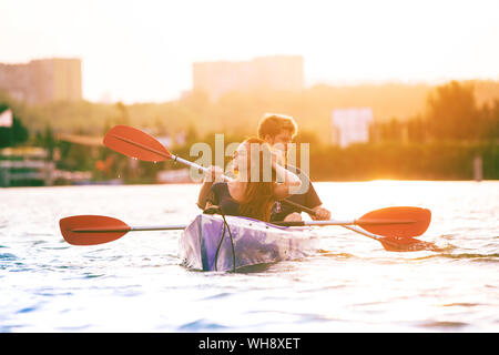 Certain young caucasian couple kayak sur rivière avec coucher du soleil dans l'arrière-plan. Avoir du plaisir dans l'activité de loisirs. Romantique et heureux homme et femme sur le kayak. Le sport, les relations concept. Banque D'Images