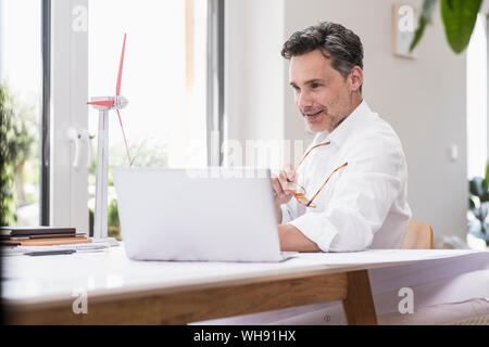 Businessma n assis dans office, en utilisant un ordinateur portable, à la recherche d'un modèle à windwheel Banque D'Images