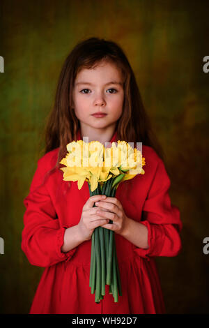 Portrait de petite fille en robe rouge avec bouquet de jonquilles Banque D'Images