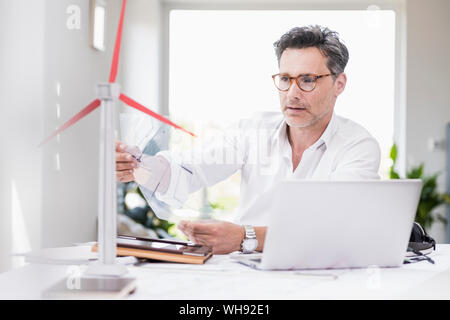 Businessma n assis dans office, en utilisant un ordinateur portable, à la recherche d'un modèle à windwheel Banque D'Images