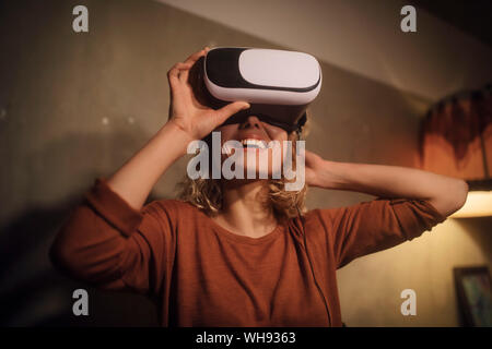 Laughing young woman putting on Virtual Reality Lunettes à la maison Banque D'Images