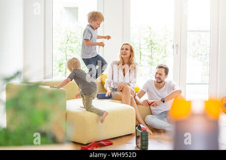 Famille heureuse dans la salle de séjour de leur nouvelle maison avec les garçons à propos de romping Banque D'Images