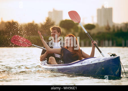 Certain young caucasian couple kayak sur rivière avec coucher du soleil dans l'arrière-plan. Avoir du plaisir dans l'activité de loisirs. Romantique et heureux homme et femme sur le kayak. Le sport, les relations concept. Banque D'Images