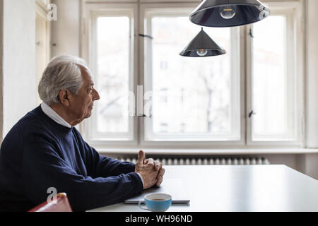 Senior man sitting at table at home Banque D'Images