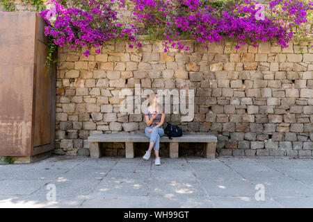 Femme avec sac à dos et de téléphones cellulaires en attente sur un banc Banque D'Images