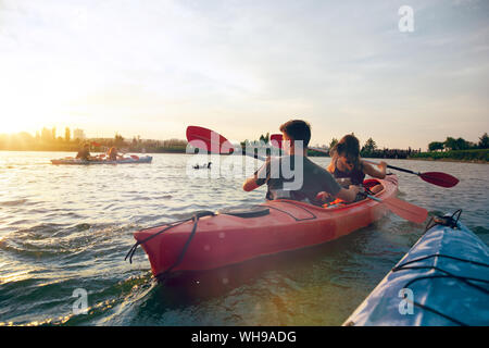 Certain young caucasian couple kayak sur rivière avec coucher du soleil dans l'arrière-plan. Avoir du plaisir dans l'activité de loisirs. Romantique et heureux homme et femme sur le kayak. Le sport, les relations concept. Banque D'Images