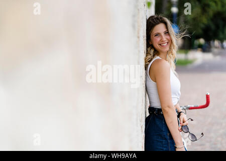 Portrait of happy young woman with sunglasses leaning against wall Banque D'Images
