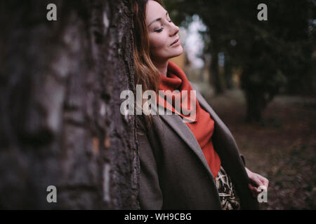 Portrait de femme aux yeux clos leaning against tree trunk portant Pull col roulé Banque D'Images