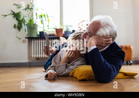 Grand-père et petit-fils gisant sur le sol à l'aide d'un comprimé Banque D'Images