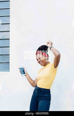 Young woman listening music casques et écouteurs avec le chant et la danse de l'avant du mur blanc Banque D'Images