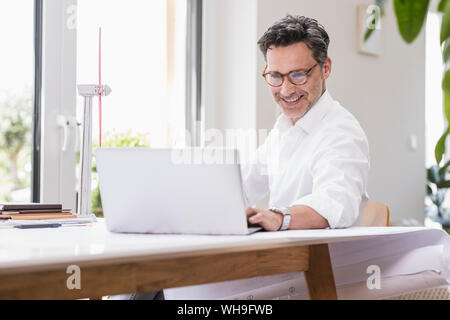 Businessma n assis dans office, en utilisant un ordinateur portable, à la recherche d'un modèle à windwheel Banque D'Images